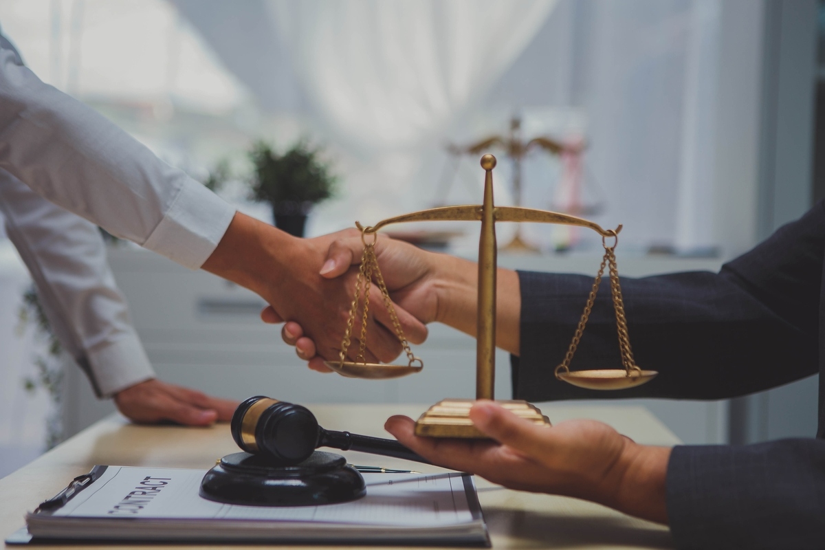 Personal injury lawyer in Queens NY shaking hands with a client next to scales of justice and a gavel