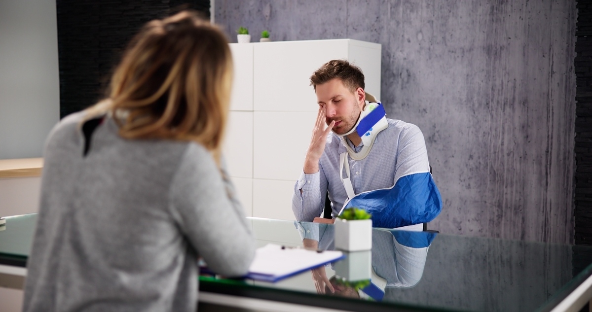 Work-site accident lawyer in Queens NY consulting with an injured worker wearing a neck brace and arm sling